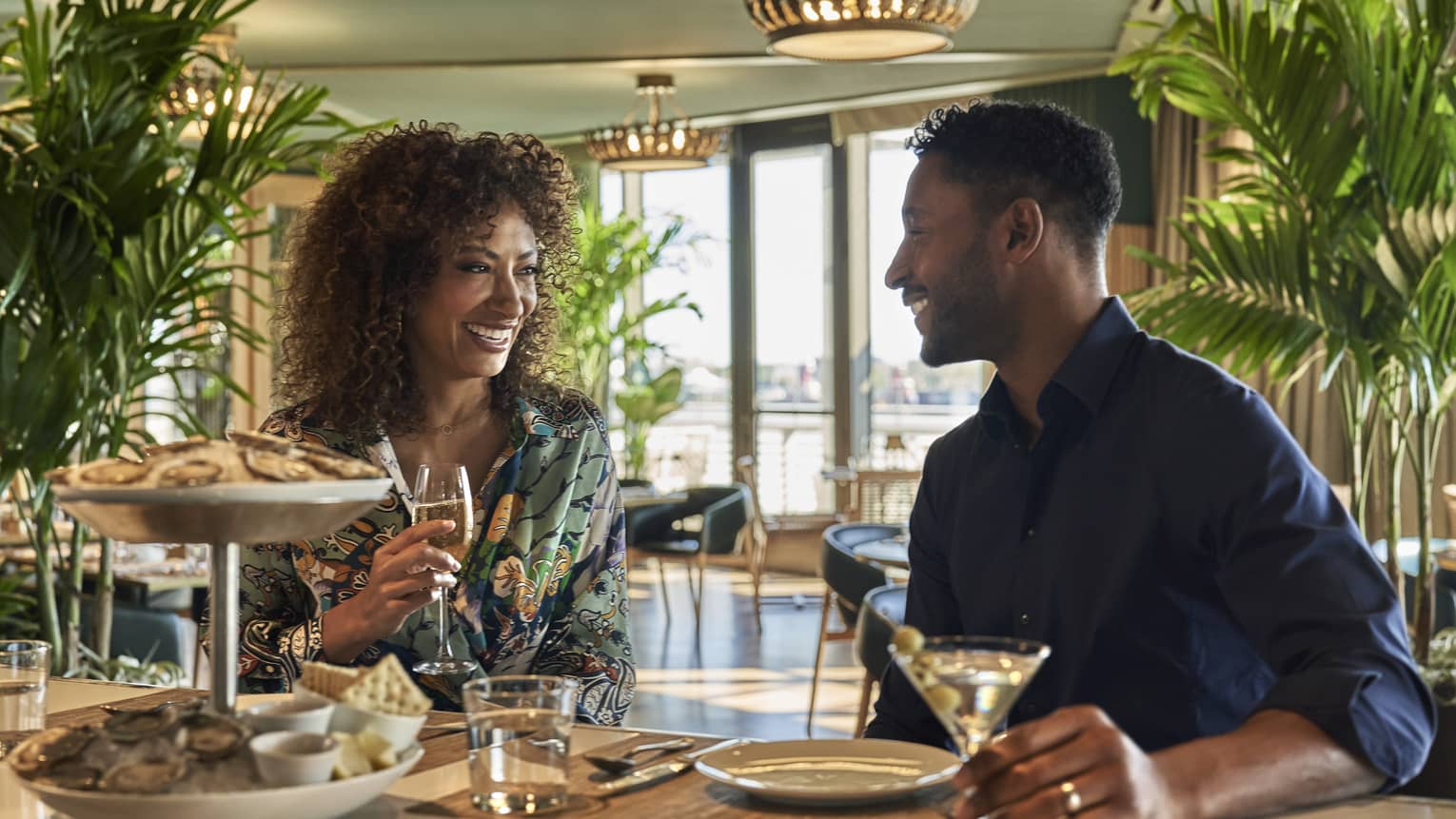 A man and woman eating oysters at an oyster bar with plants behind them.