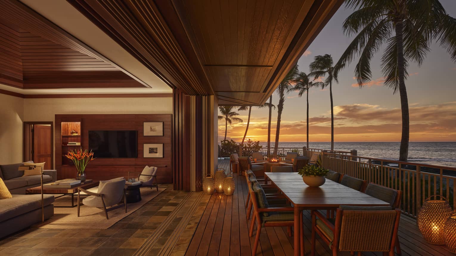 Private villa's living room opens to an outdoor wooden deck with dining table at sunset