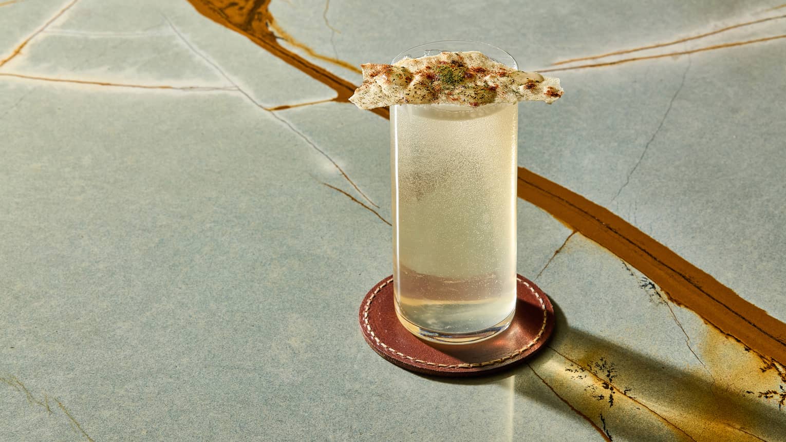 Light-coloured cocktail in a highball glass set on a marble table