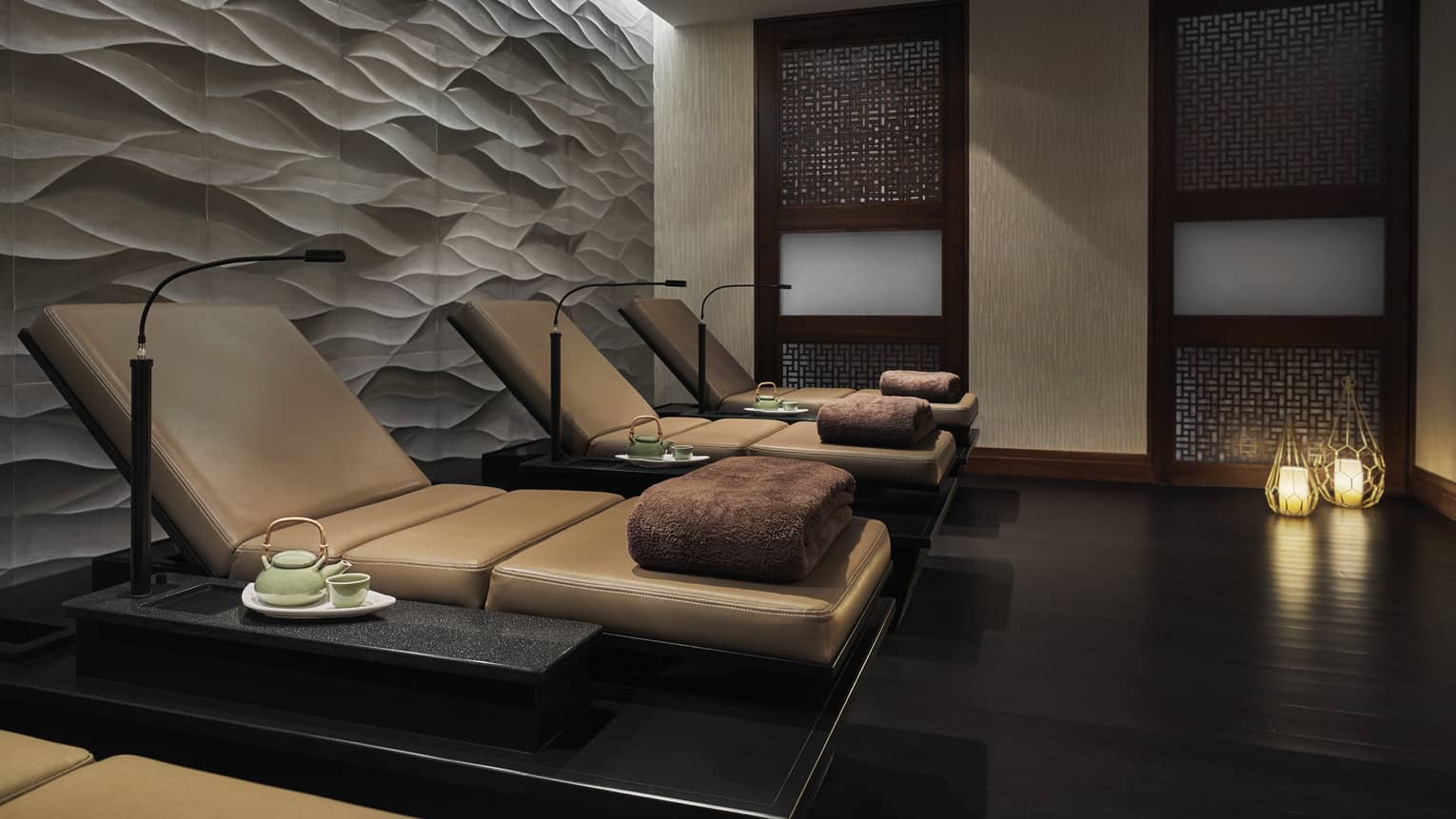 Several lounge chairs with large brown towels placed atop them in a stone room.