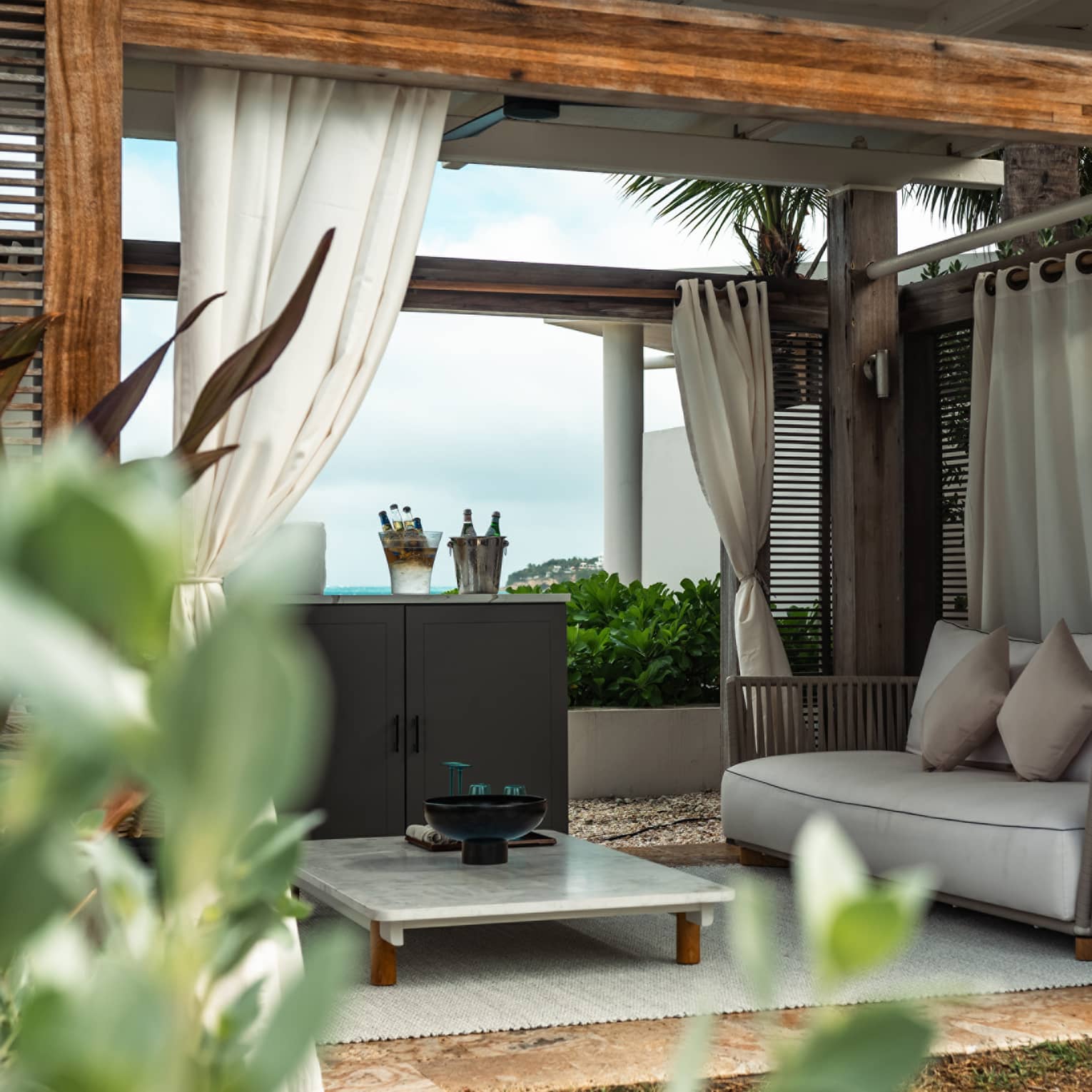 A cabana with a marble table and couch surrounded by palm trees