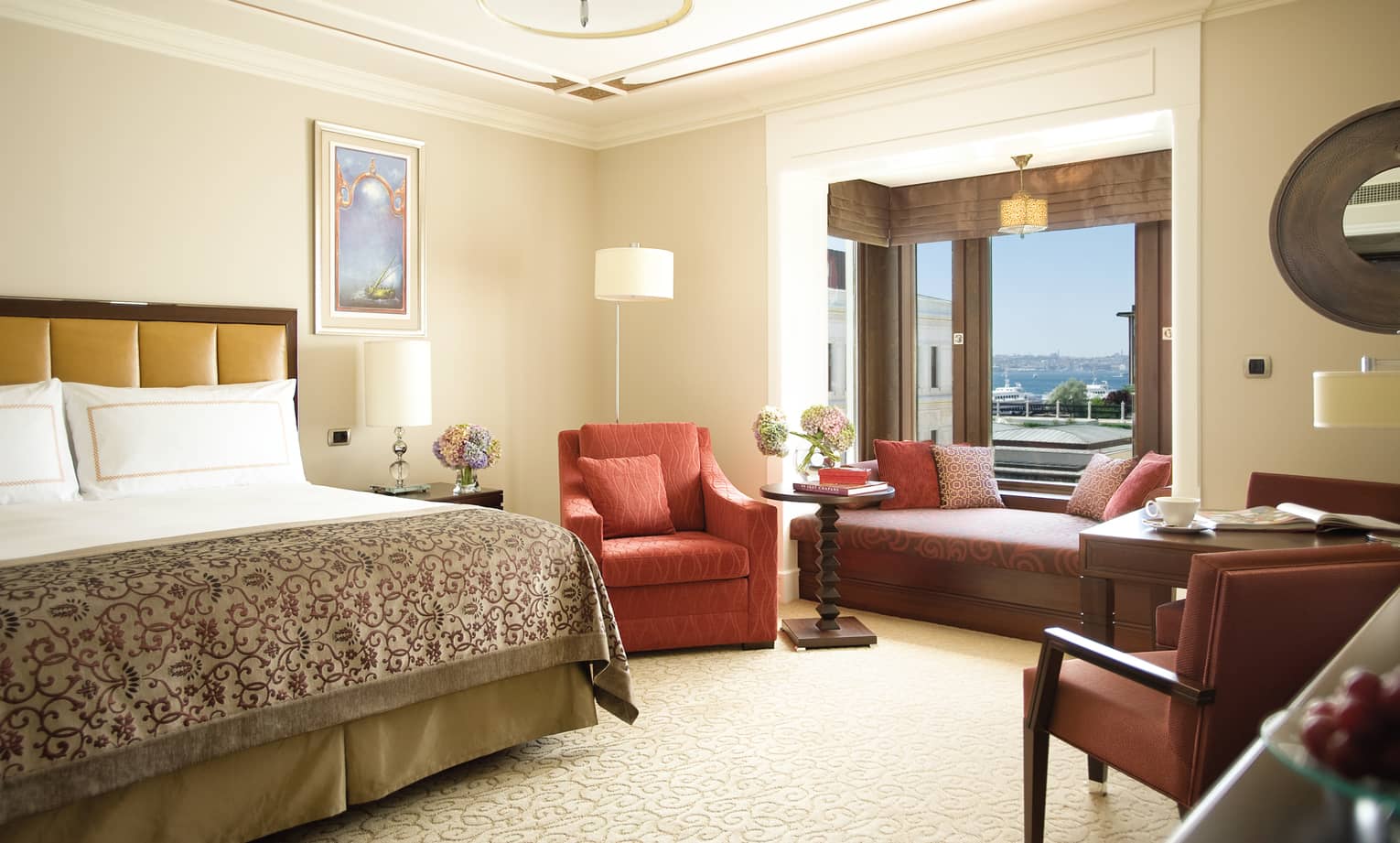 Deluxe Room bed with patterned blanket, red armchair, padded bench under window