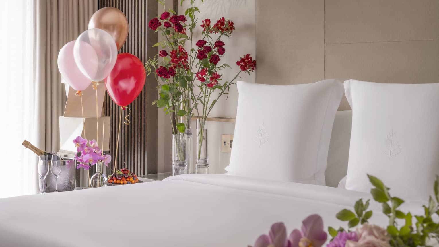 King bed with white linens surrounded by colourful balloons and ice bucket of champagne nearby