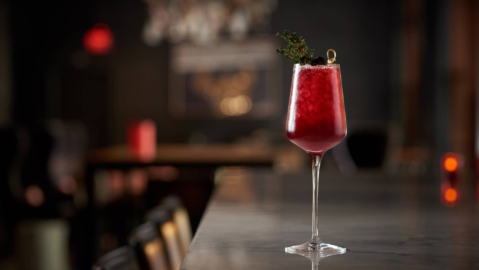 A red cocktail sitting on a dimly lit bar.