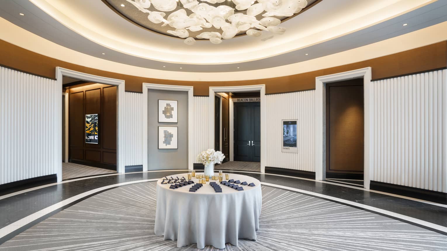 Lobby pre-function are with chandelier, uplighting, round table in middle, grey & gold accents