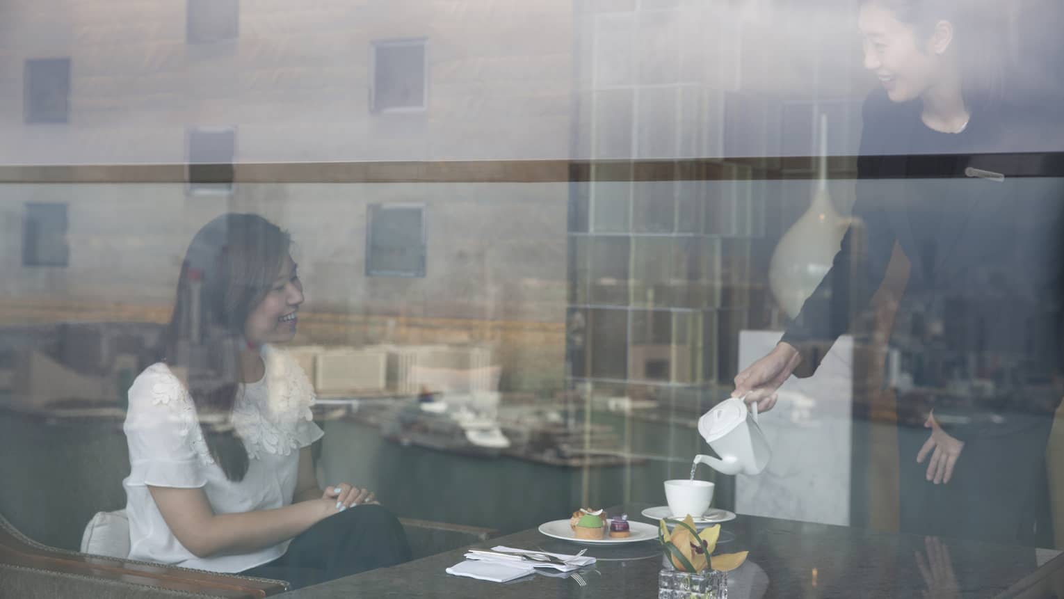 Woman is served food and tea, as seen through glass wall