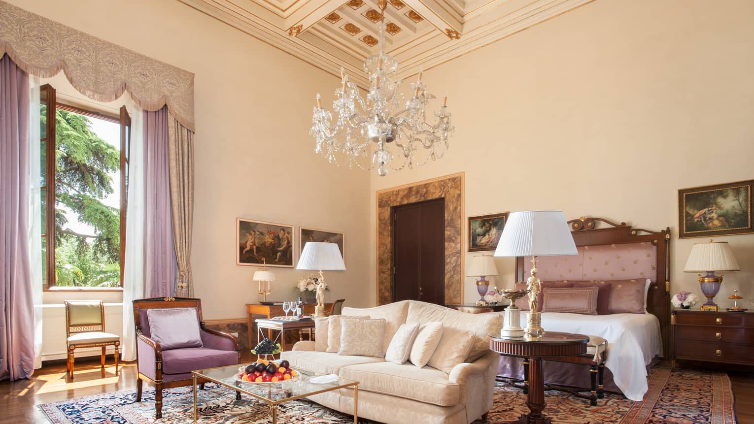 Gallery Suite white sofa, purple armchair, bed under large crystal chandelier, high ceiling