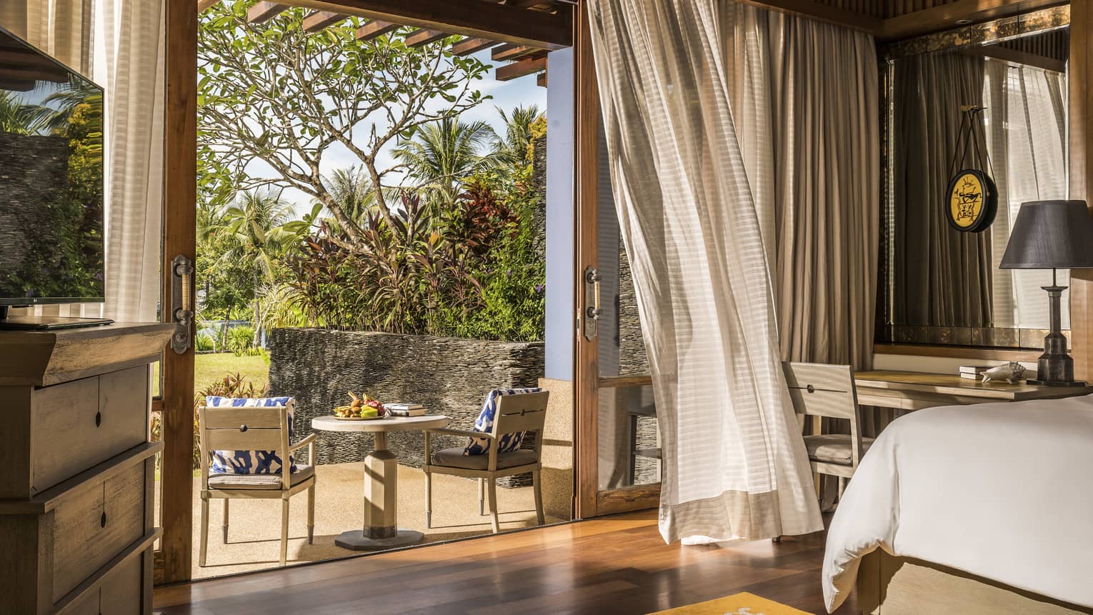 A neutral bed room with sliding glass doors opened to an outdoor patio.