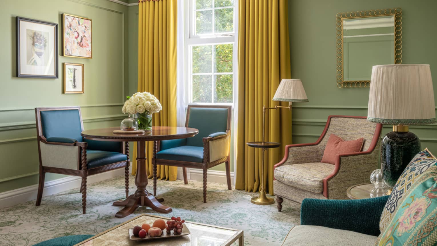 Guest room with cream accent chair, small round table with two leather dining chairs, avocado-coloured walls, window with yellow drapes