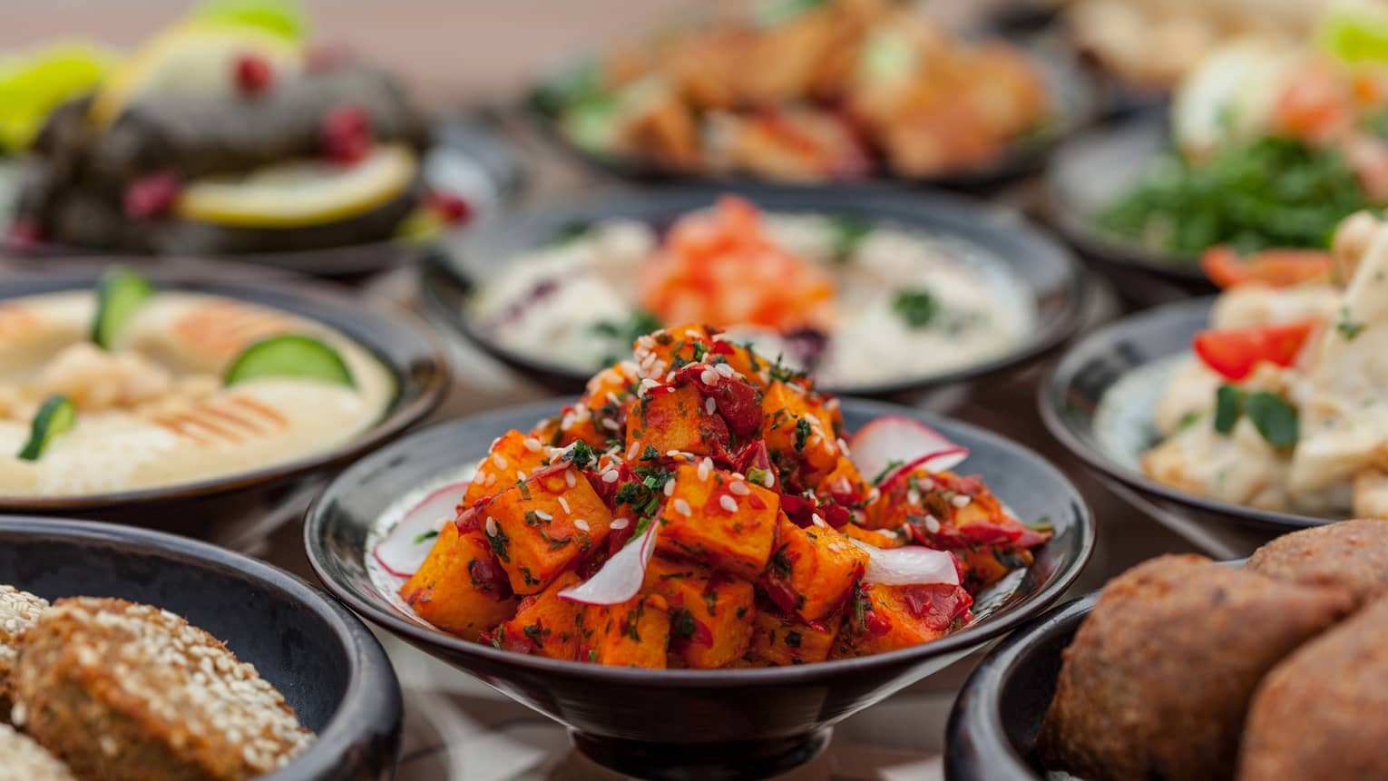 Several black plates filled with meat and vegetable appetisers.