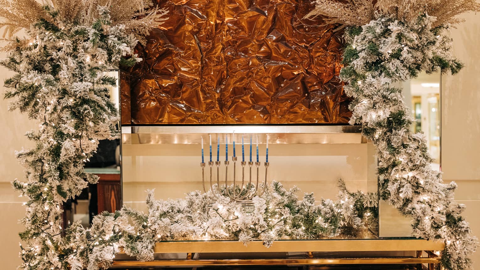 Menorah set up on a golden table surrounded by holiday garlands