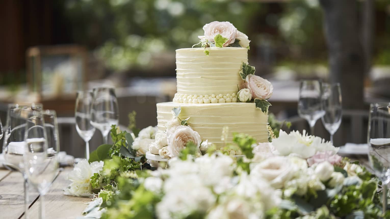 Two-tiered white wedding cake on banquet table with wine glasses, flowers