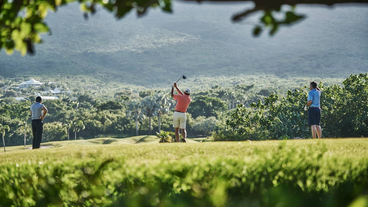 Back of three people standing on Robert Trent Jones II Golf Course, man swings golf club