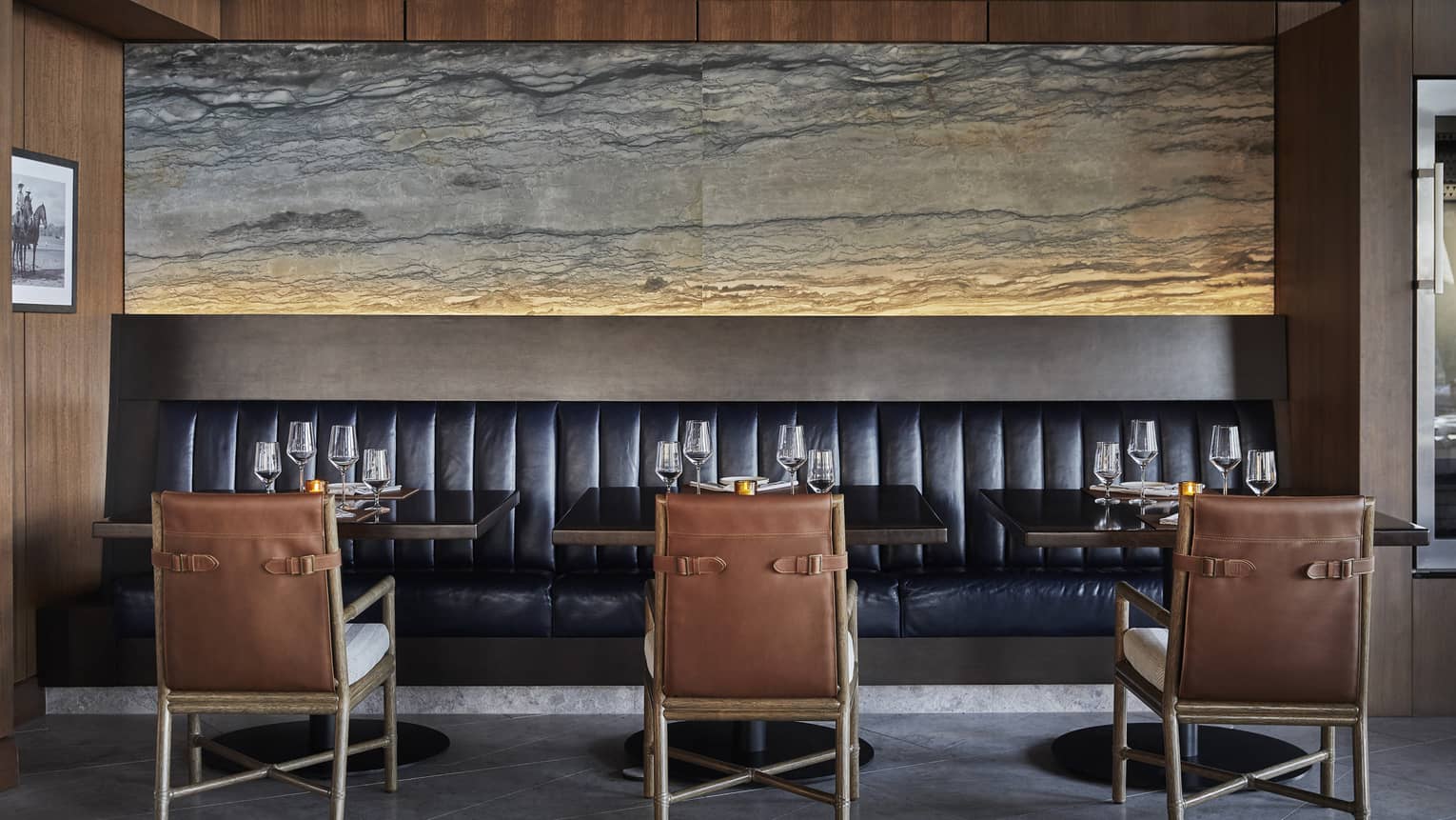 Three brown chairs face a black booth in a dining room.