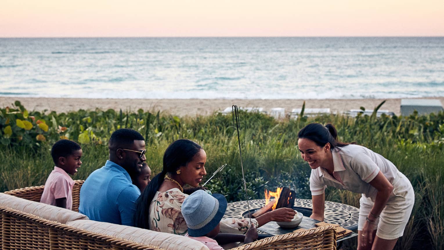A family with a husband, wife, and two children talking to a staff member while the cook s'mores outside near water.