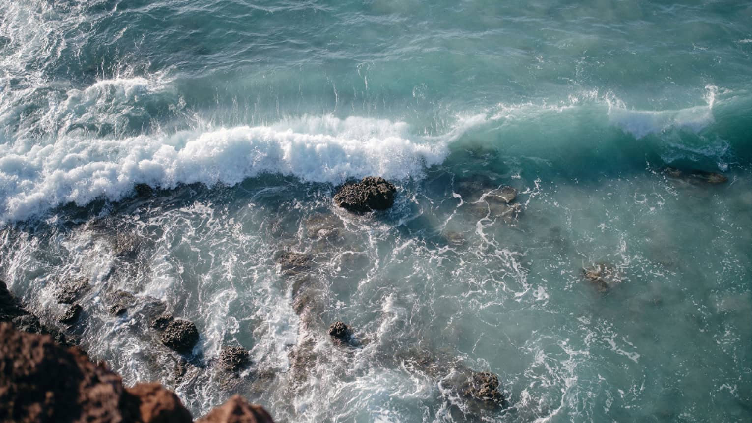Aerial view of an ocean wave breaking over a rock formation