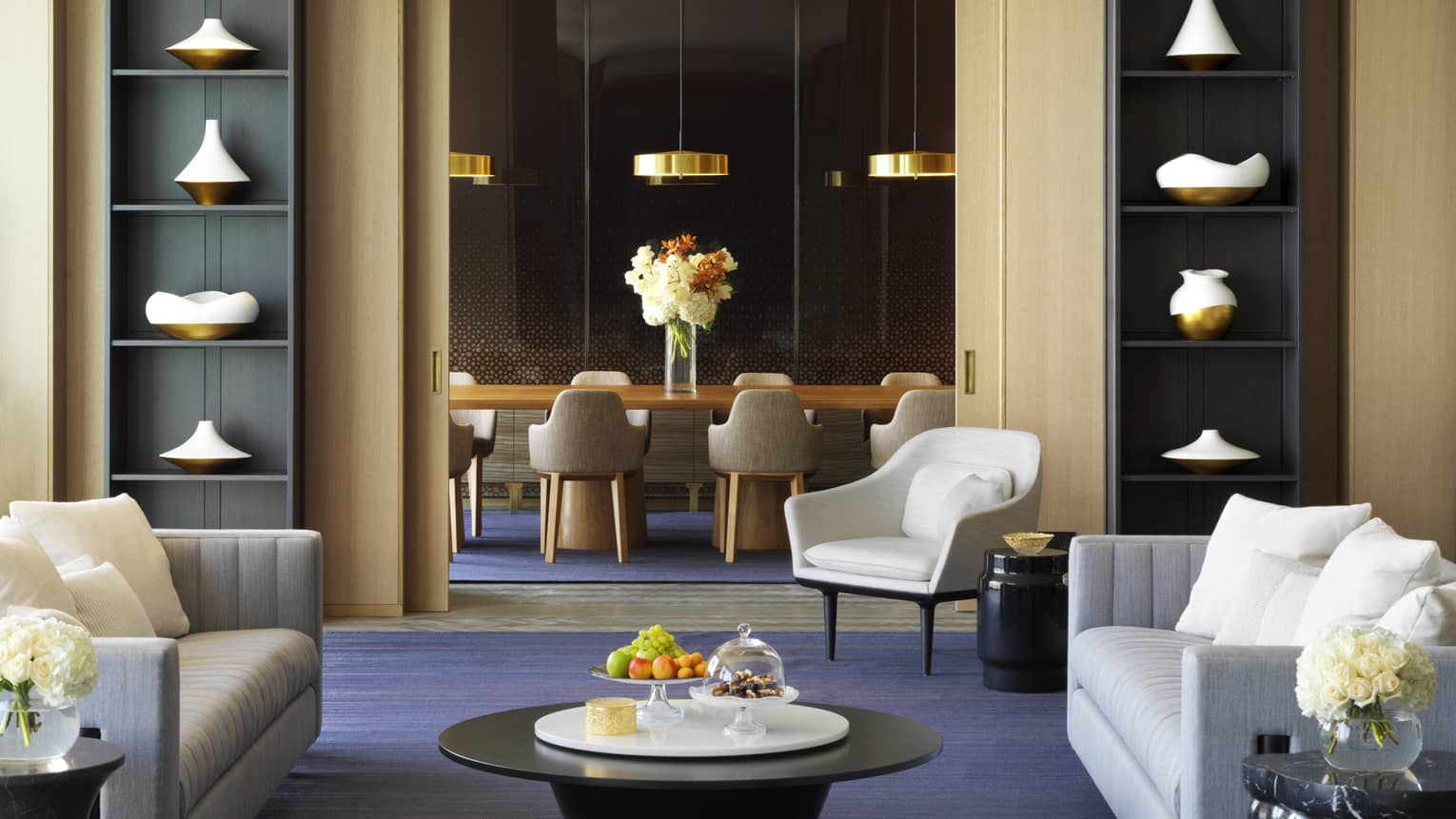 Modern dining table, gold lamps in private room behind lounge with tall bookshelves, sofas