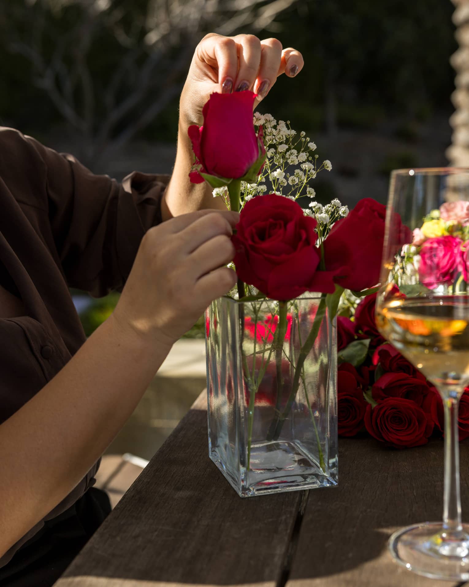 Person's hands arranging three stems of red roses in a glass vase with springs of baby's breath