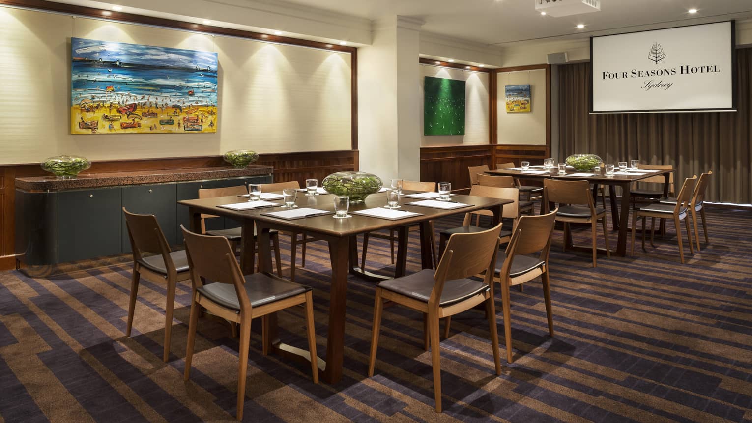 Gallery meeting room with small square tables with retro-style chairs, colourful paintings on walls