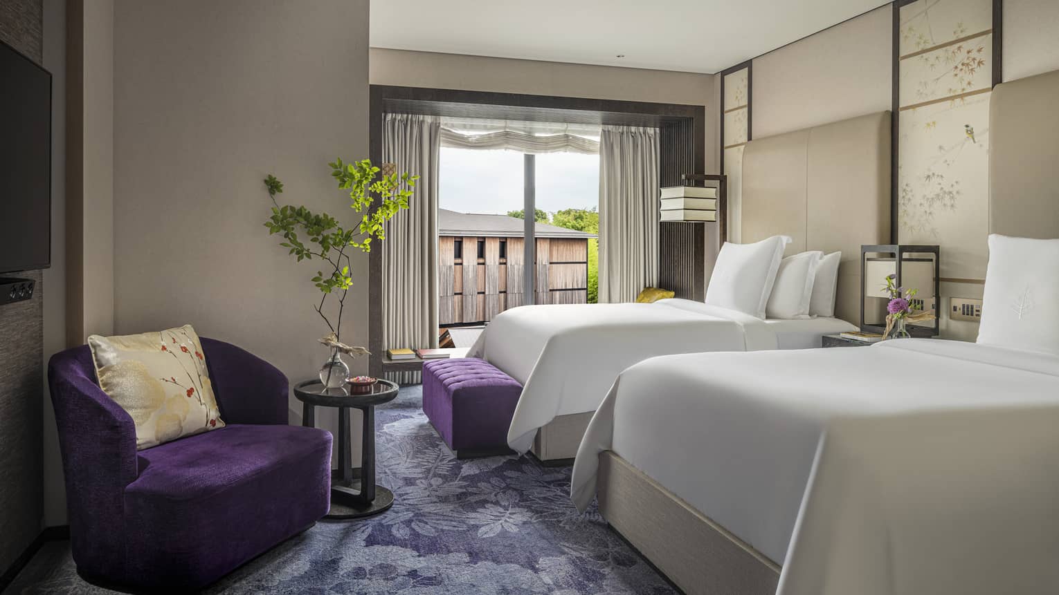 Hotel room with two beds, a purple armchair, green plant on a side table and a large window with a balcony view