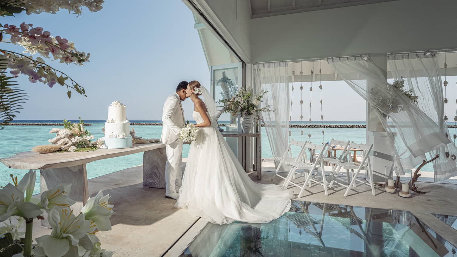 Bride whispers in groom?s ear in the glass-bottom overwater wedding pavilion