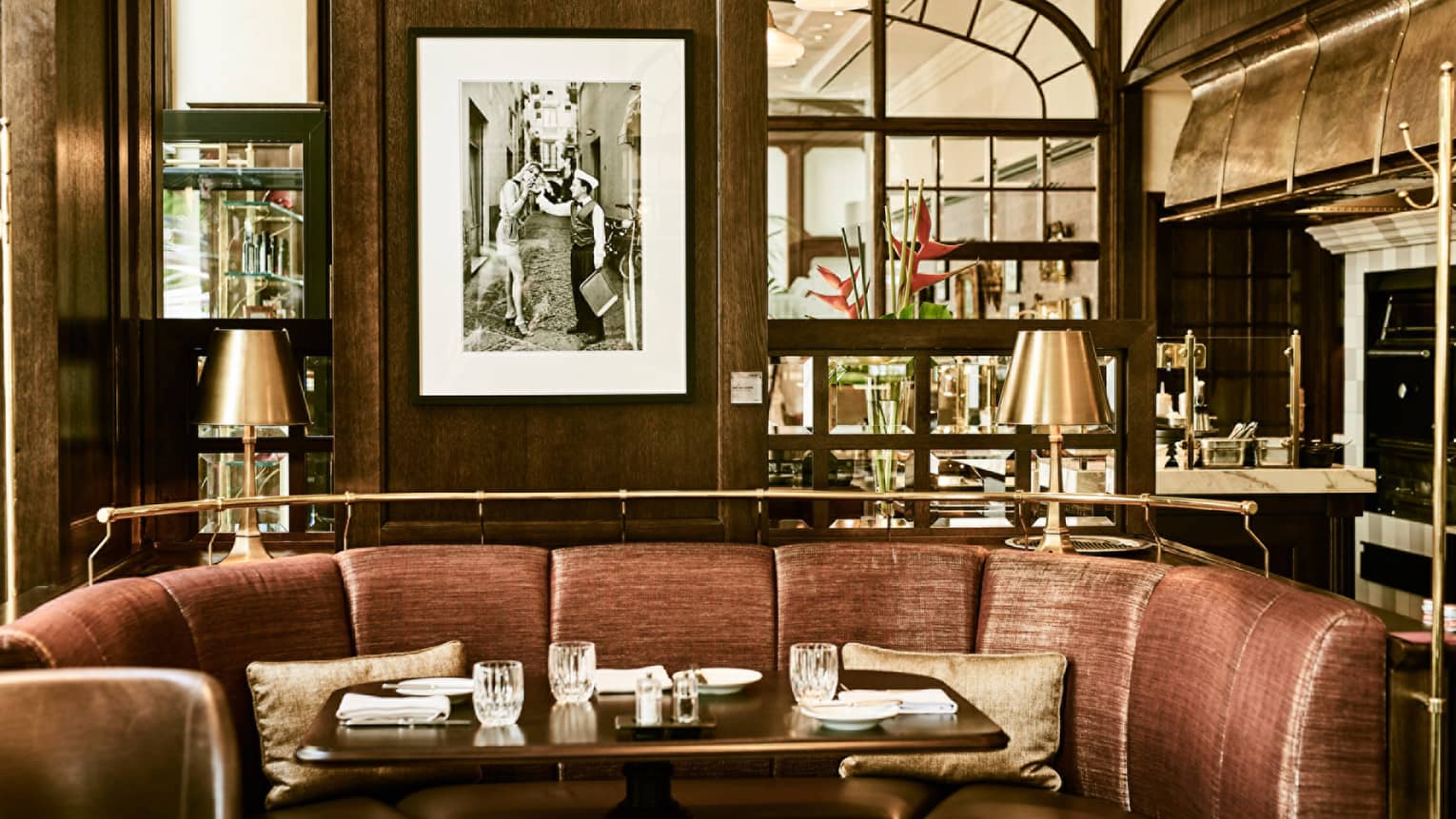 KOLLÁZS Brasserie & Bar curved brown booth, dark wood walls, black-and-white art, gold lamp