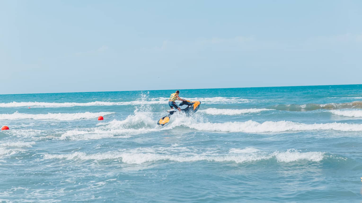 Person riding jet ski along waves in blue ocean