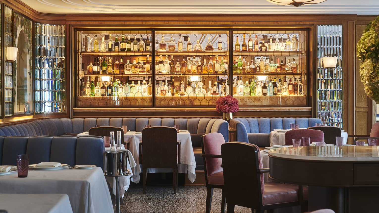 Fine dining restaurant with a stocked bar, upholstered seating, tables set with white tablecloths and warm ambient lighting