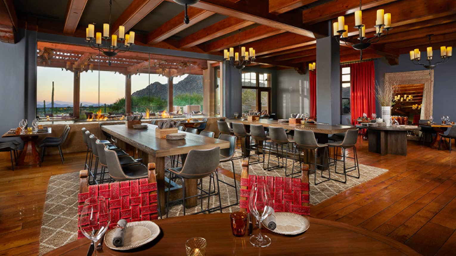 Indoor restaurant with long tables, wooden ceiling beams and wooden floors, candle-like chandeliers
