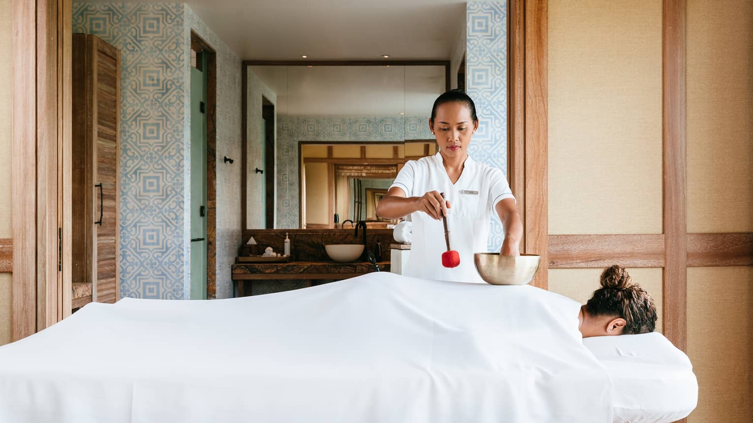 Spa staff pours oil on woman's back who is face down on massage table 