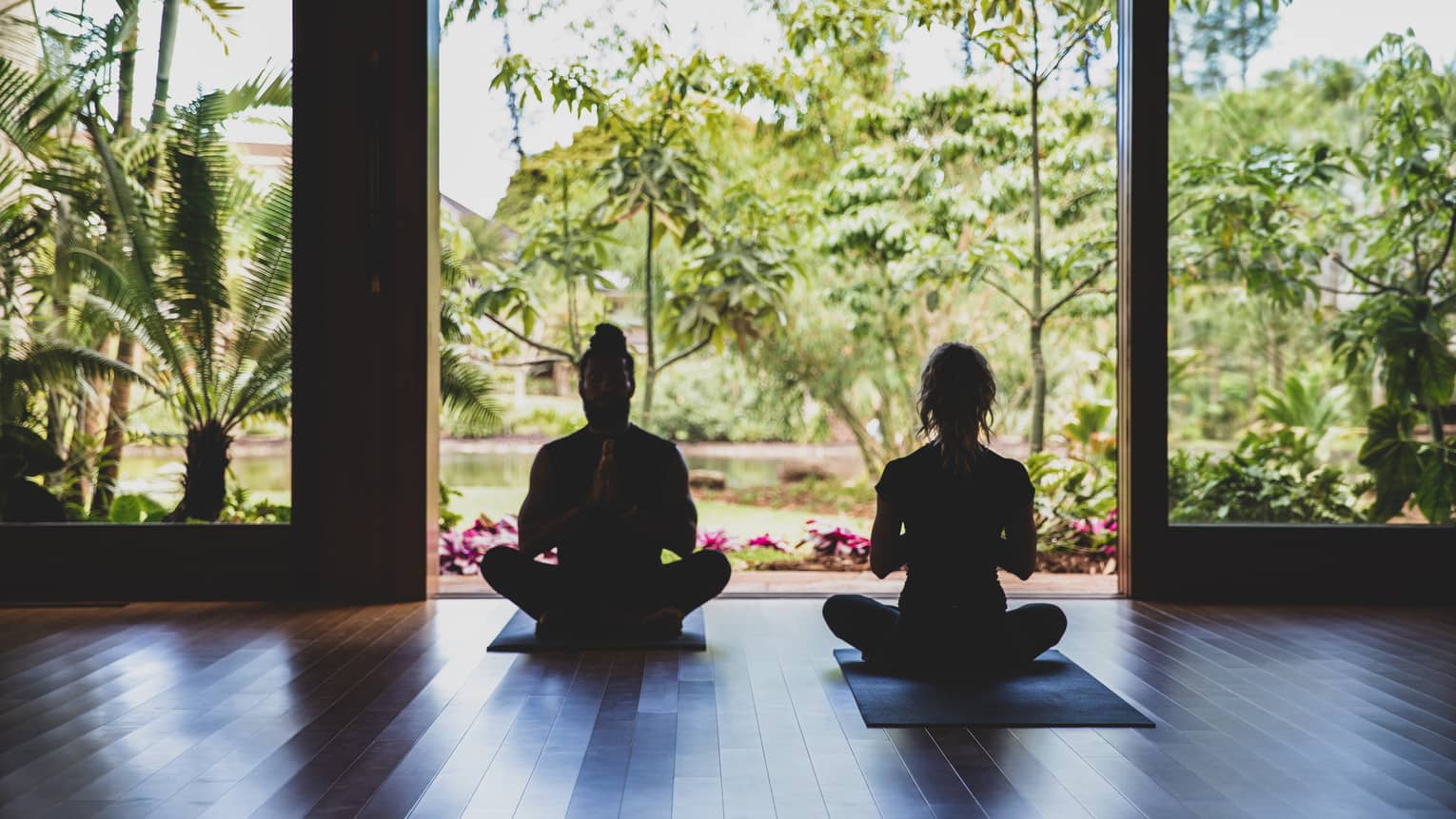 Two people practice yoga in the outdoor covered pavilion surrounded by greenery