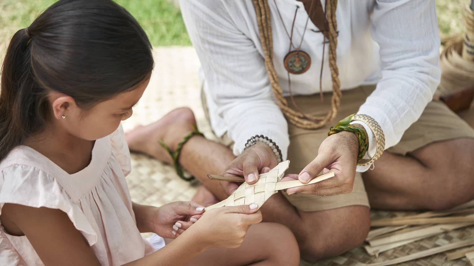 An adult shows a young girl how to weave a basket