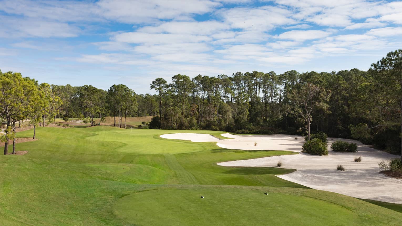 The sky is blue over a green golf course with sand dunes