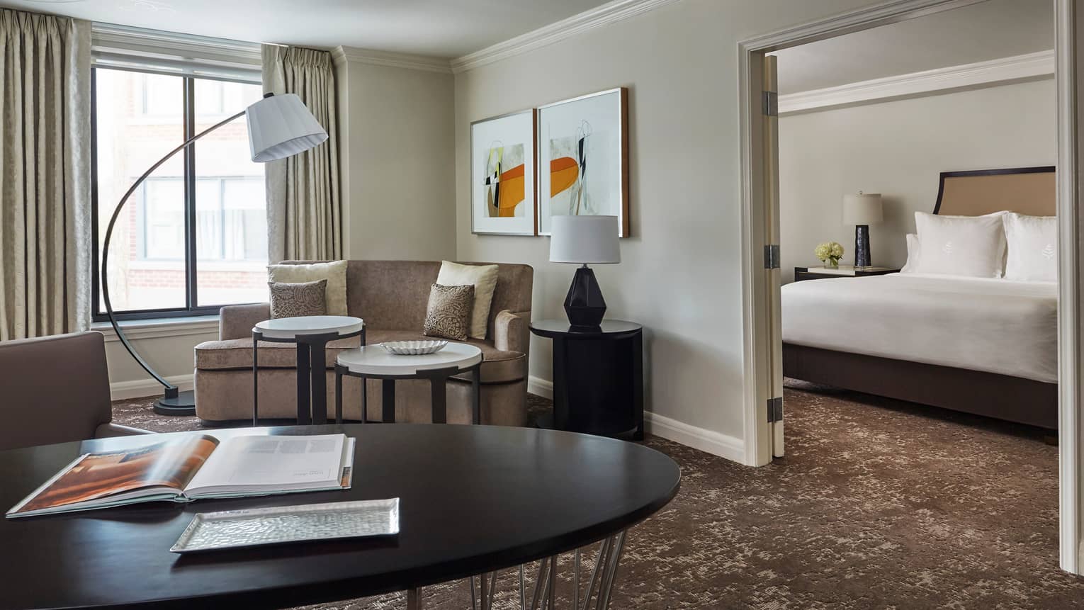 Premier Suite large black table in front of curved loveseat, open French doors to bedroom, bed