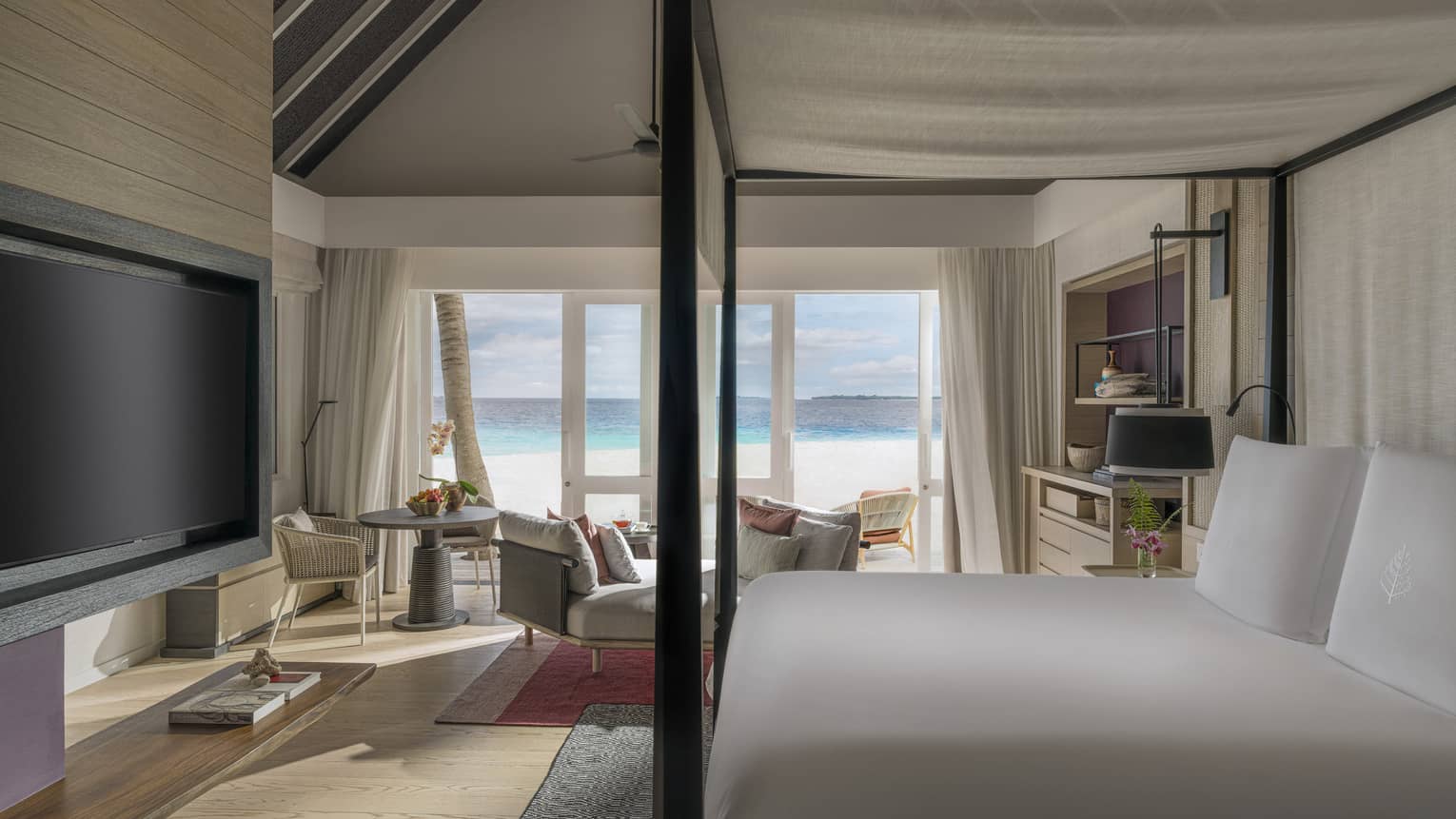 Luxury resort bedroom with four-post king bed, TV, sitting area and walk-out beachfront terrace