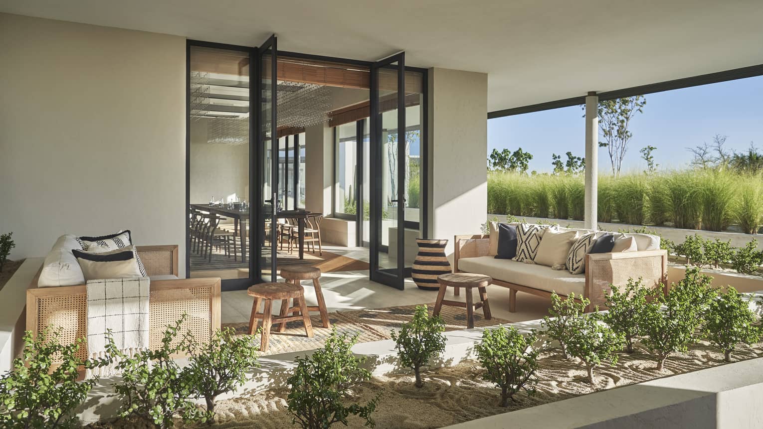 A modern Cortez opens up to a covered terrace furnished with natural wood and white couches, wooden rattan chairs and shrubbery 