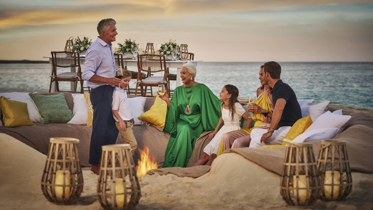 People enjoying a sunset gathering around a beach fire pit, with cozy seating and ocean view