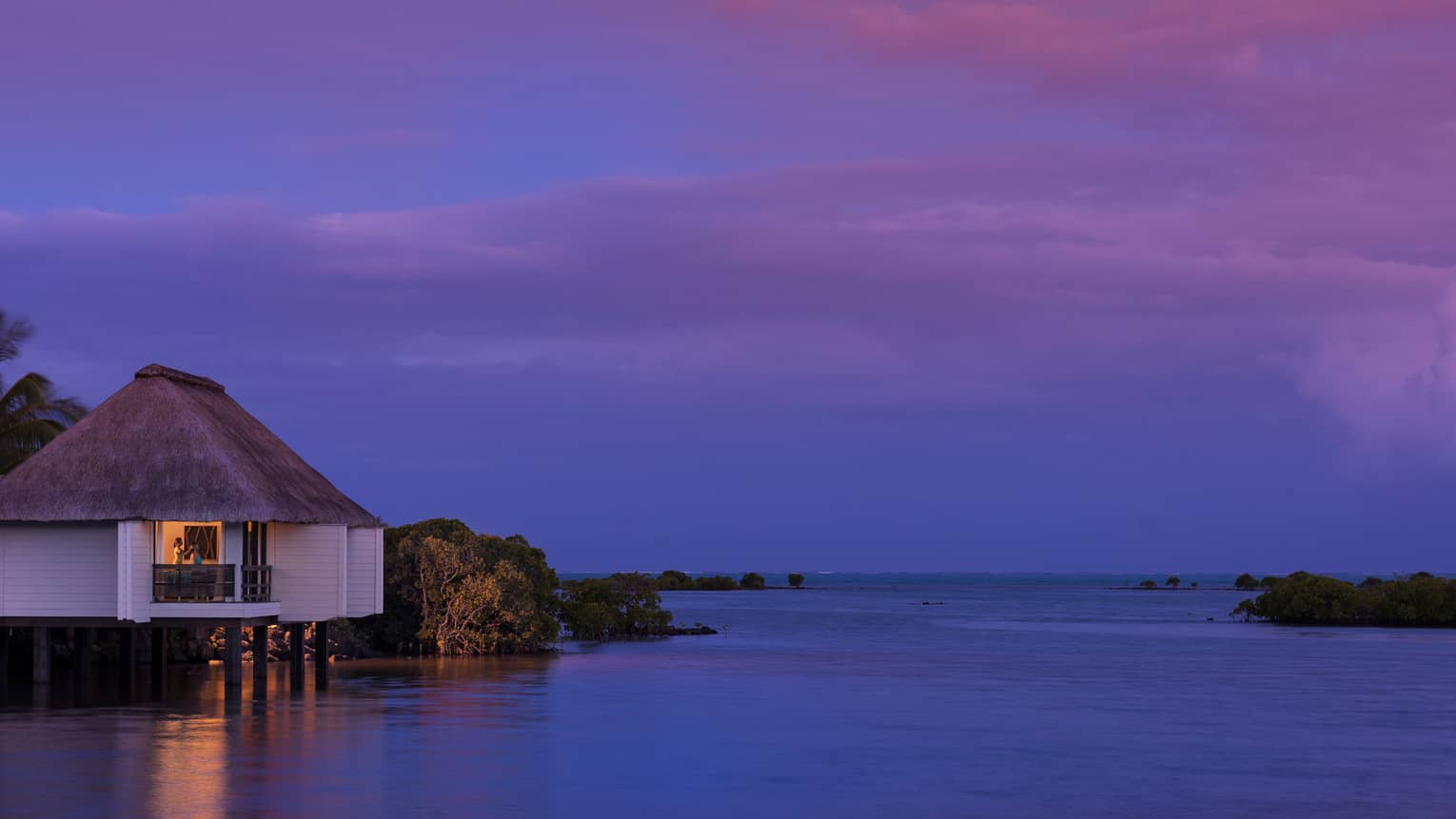 Spa staff massaging woman's head on deck of small white villa over water at night