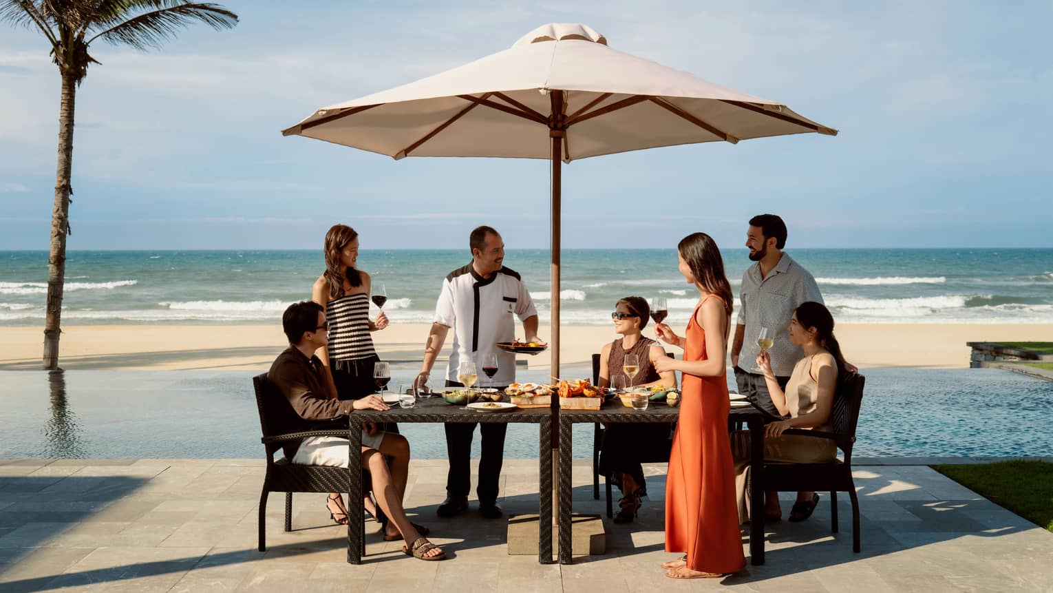 Friends gathered at a table with food setup and view of pool and beach in background