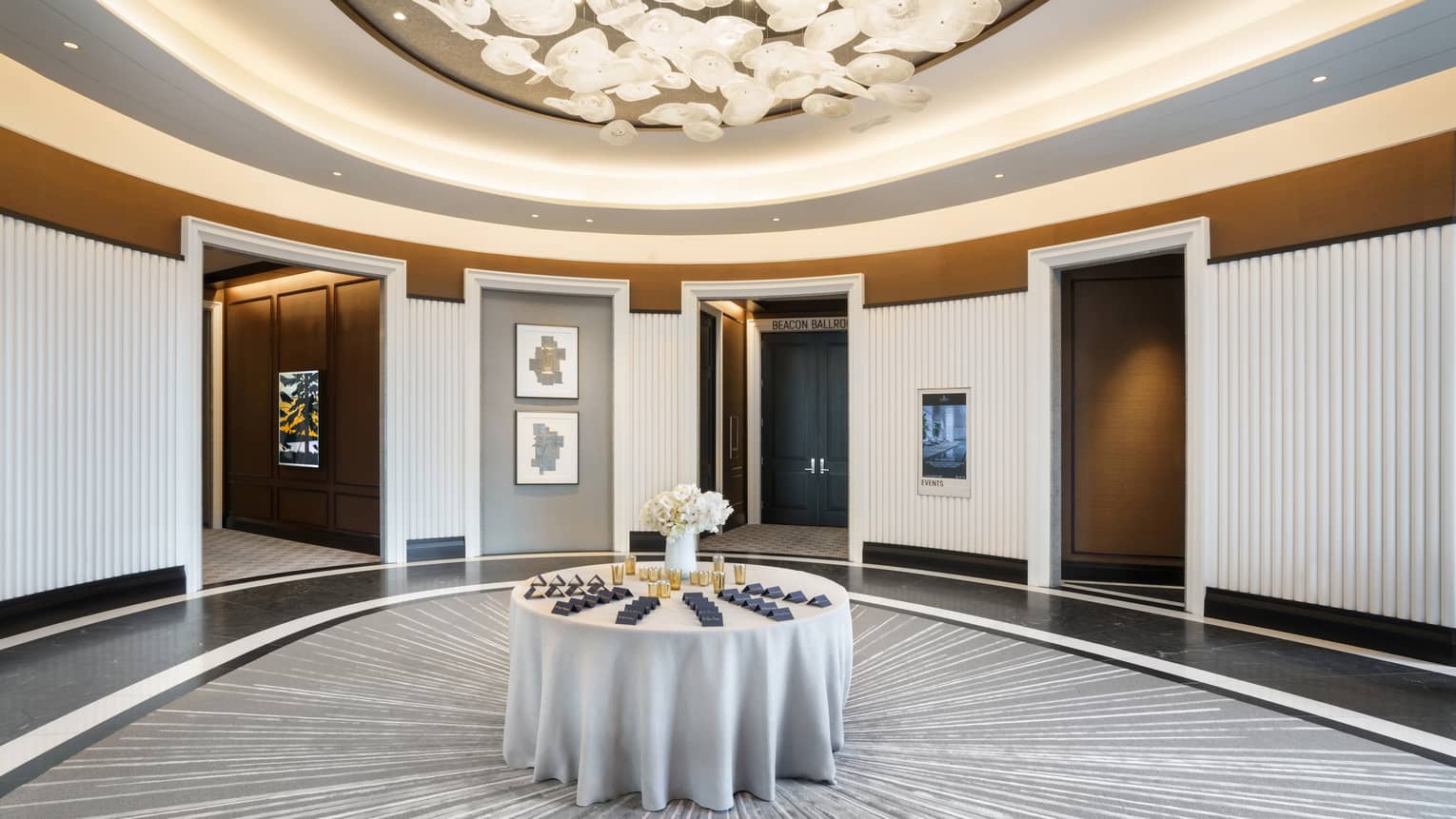 Lobby pre-function are with chandelier, uplighting, round table in middle, grey & gold accents