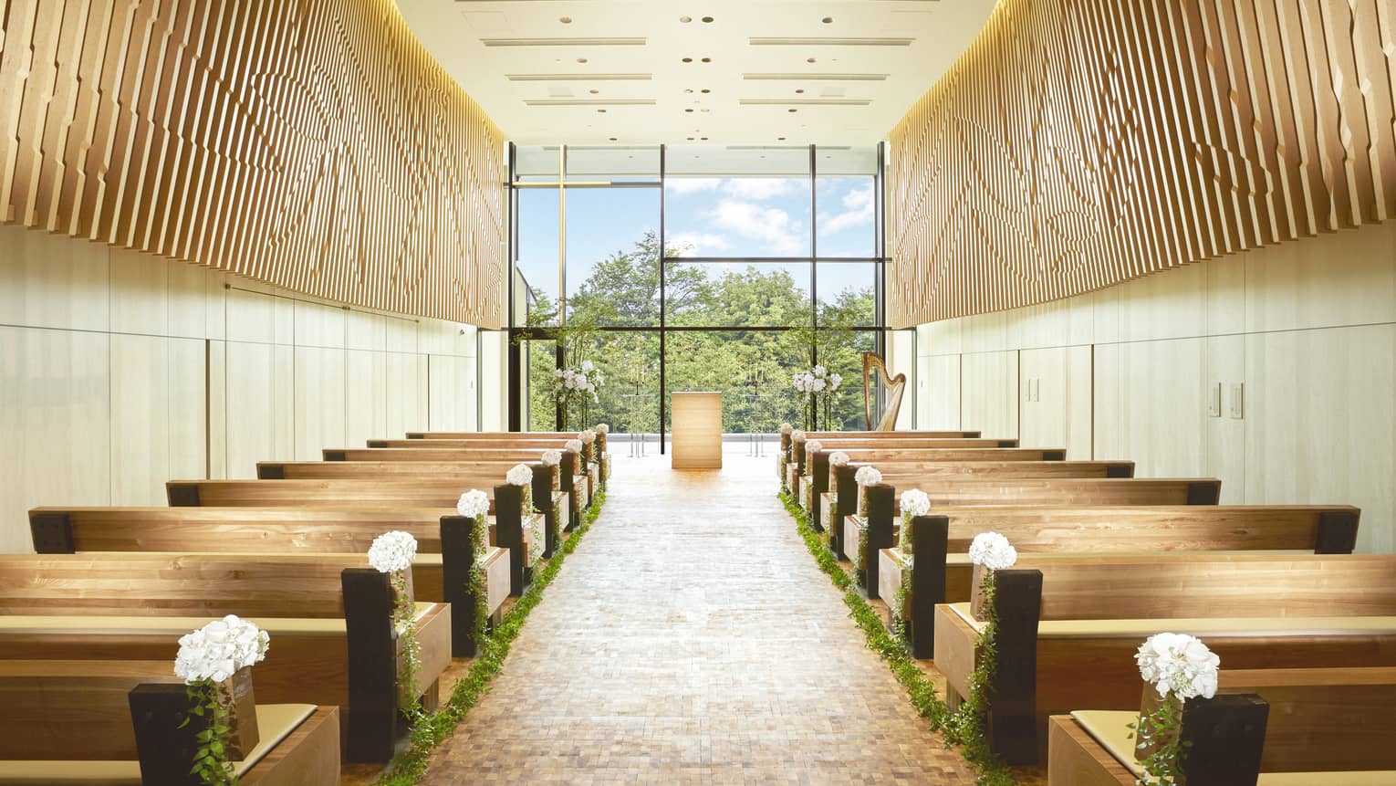 Rows of pews on either side of aisle, floor-to-ceiling window in in bright, modern chapel
