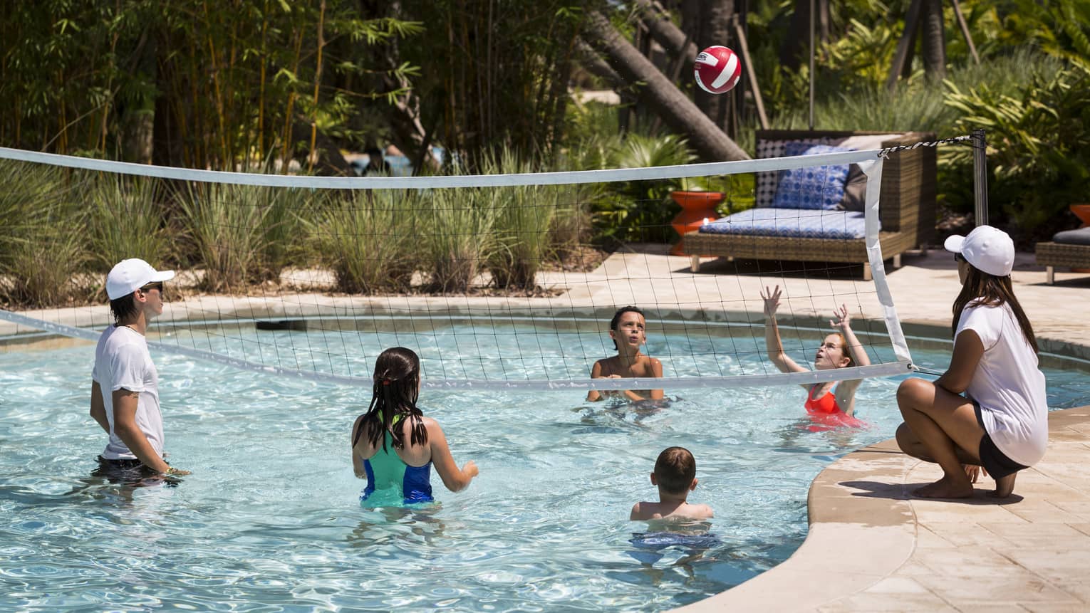 Kids play volleyball in small outdoor swimming pool with net