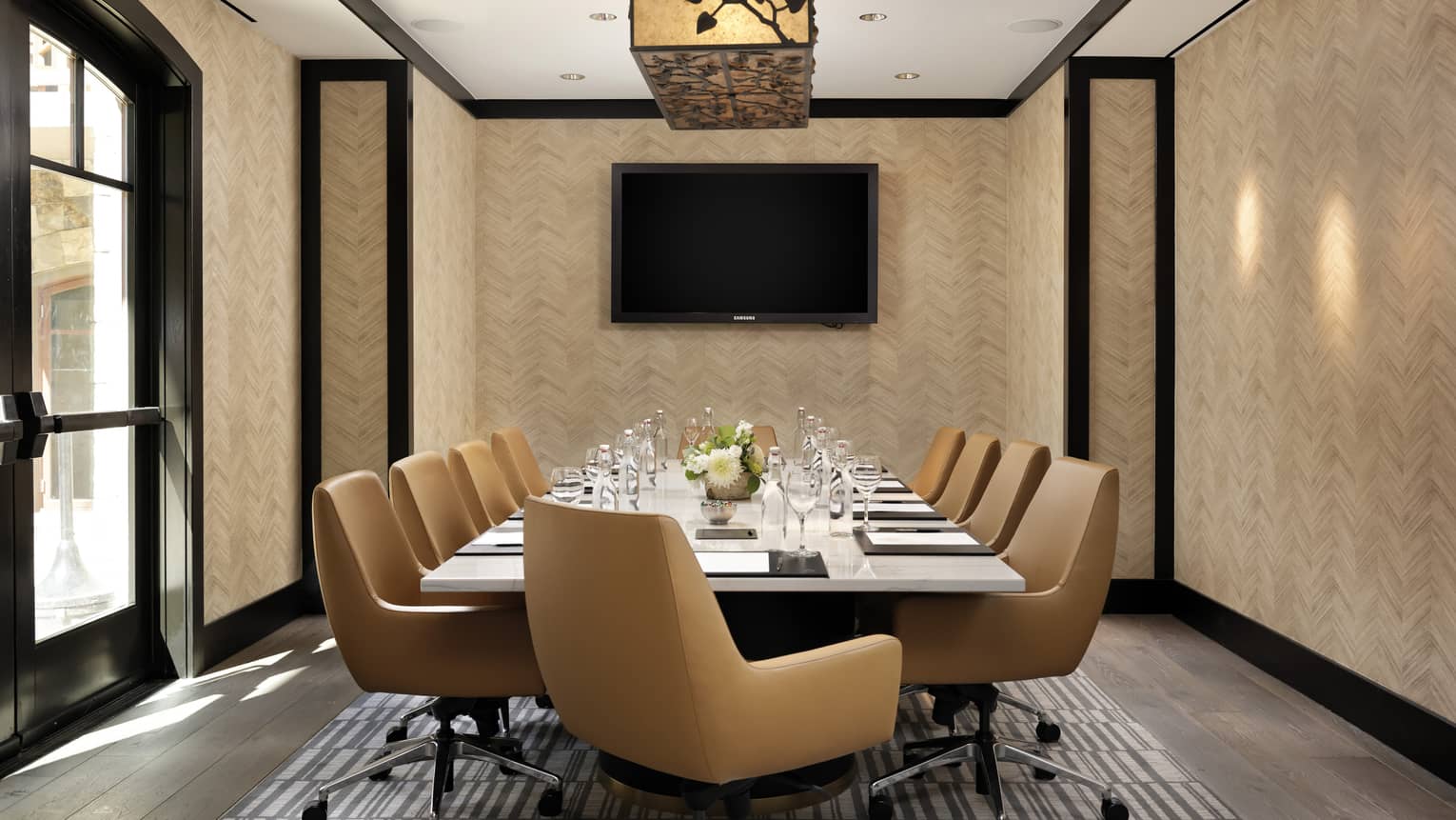 A meeting room with a monitor on the wall and rolling chairs lining the table