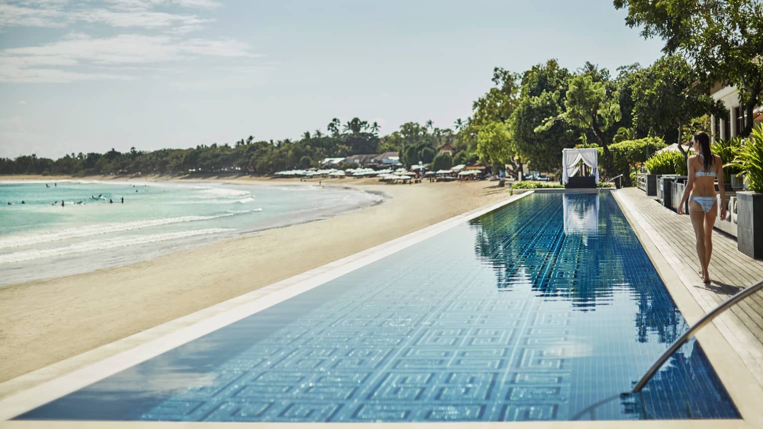 Woman in bikini walks by long Sundara infinity swimming pool over white sand beach