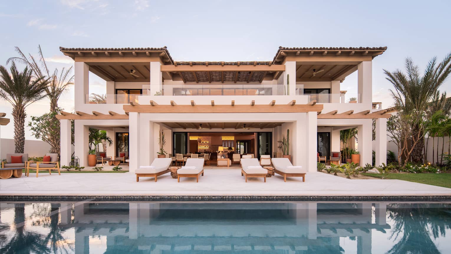 Spanish-style, two-storey villa lined by palm trees and sert behind a pool and deck