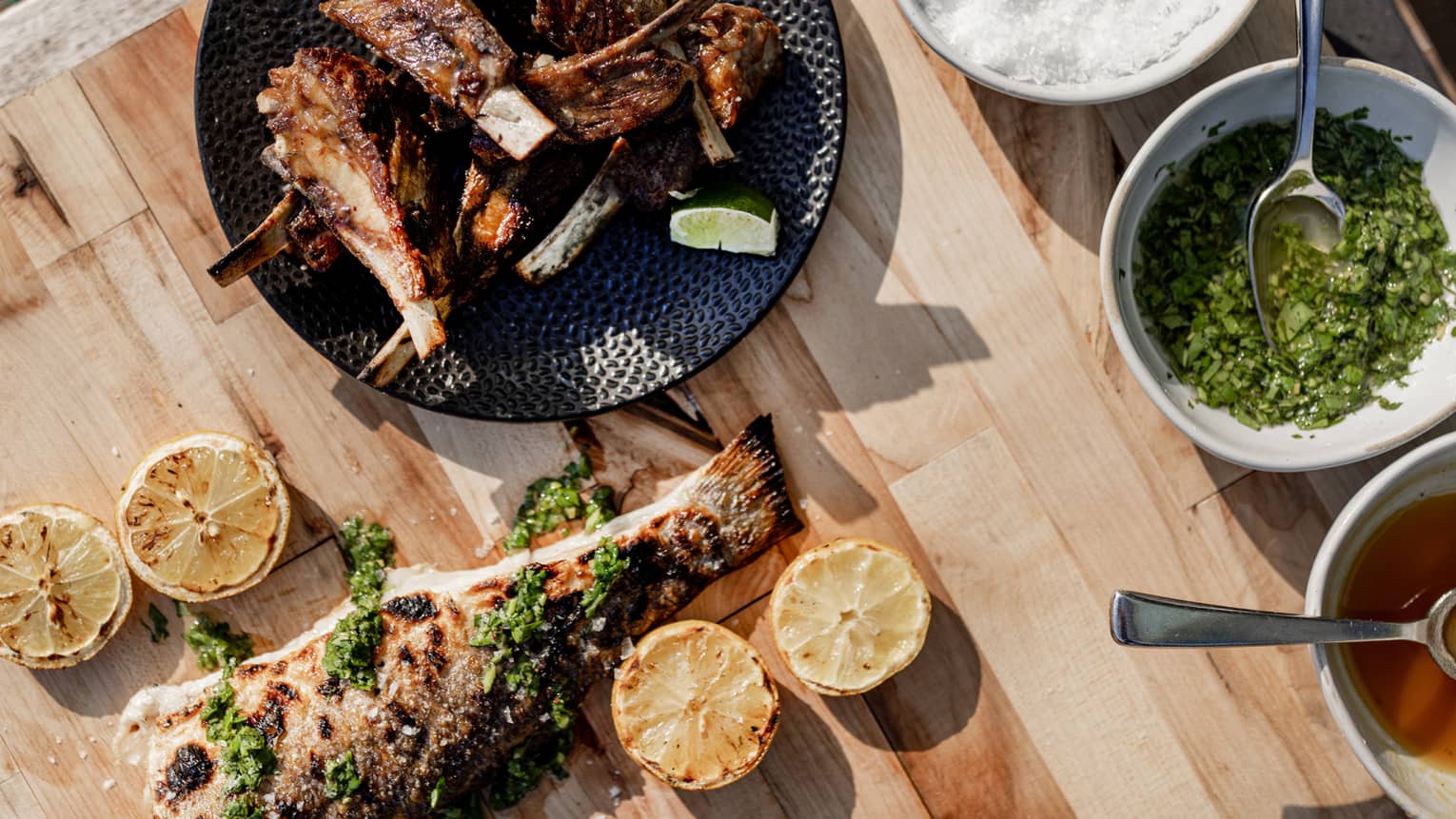 Fish on a wood table near a black plate of ribs.