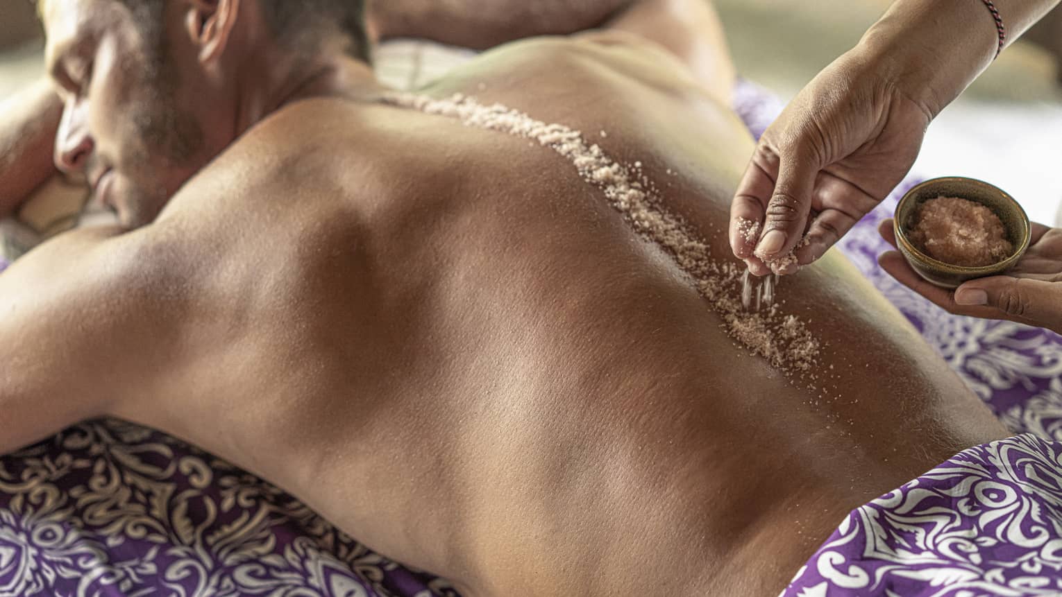 Hand place spa salts along man's spice during Sacred River Spa Massage