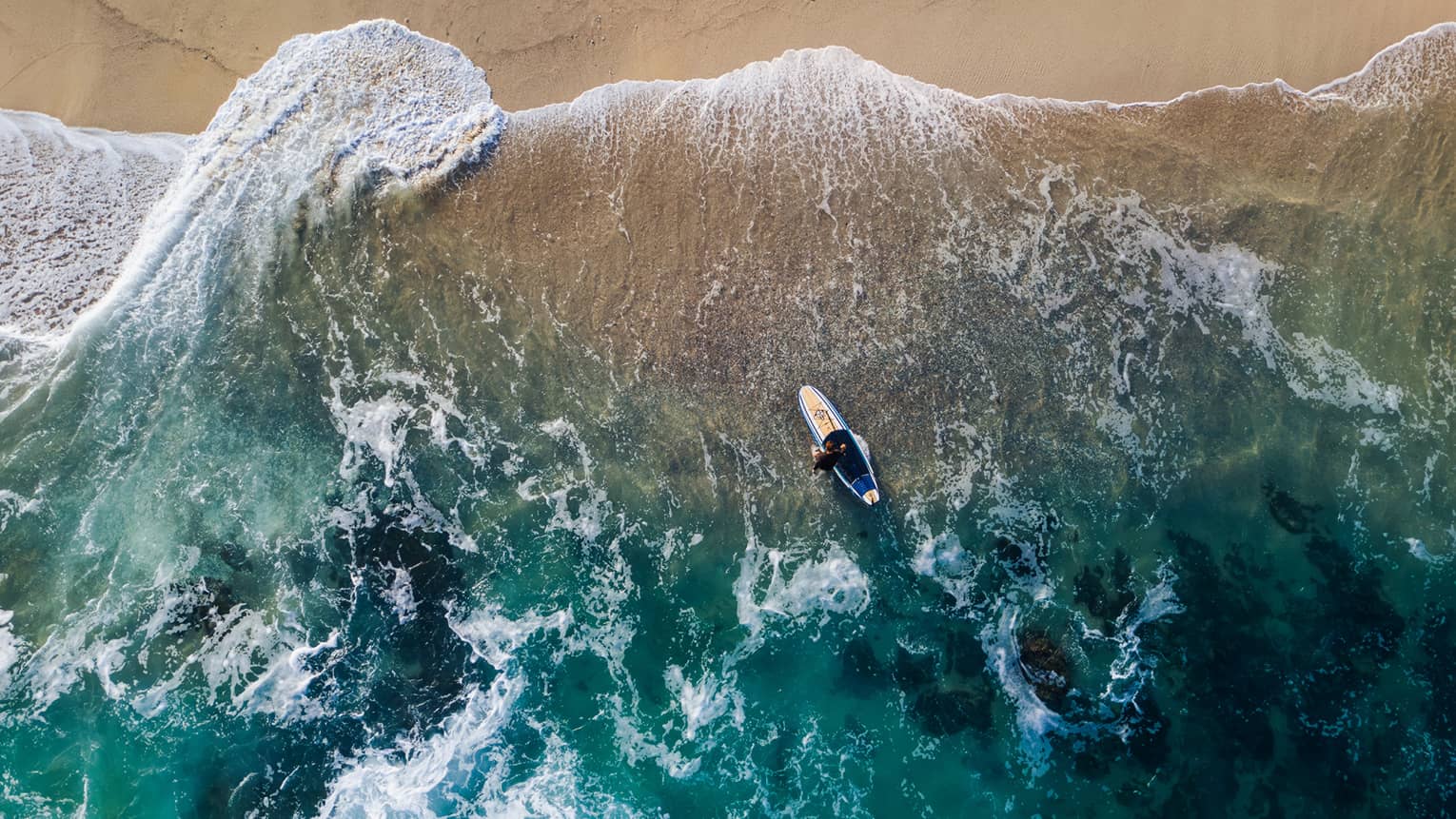 Aerial view of a person paddle boarding in the ocean by the beach