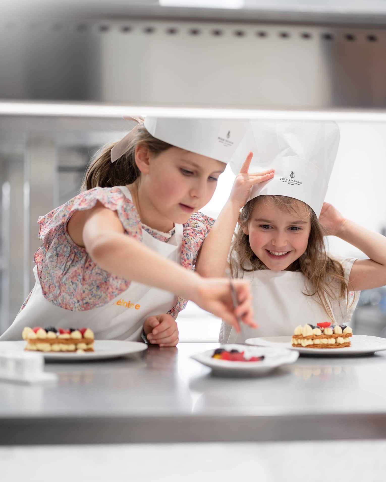 Two young children wearing Four Seasons chef hats work on dessert creations at a cooking class in a Four Seasons kitchen