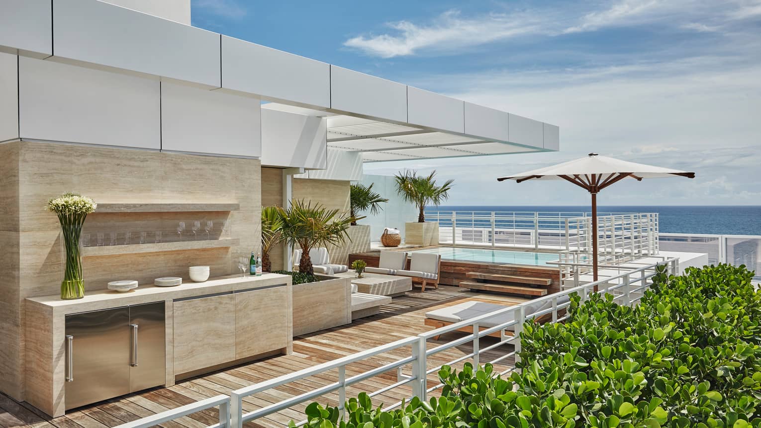 Marble outdoor bar and kitchenette with glasses, flowers, white sofas on modern rooftop patio with ocean views